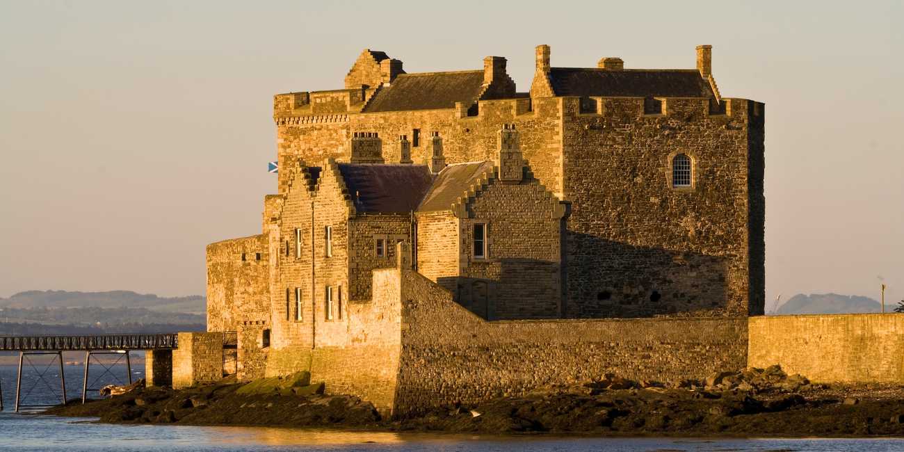 Scenic view of Blackness Castle sitting directly on the shores of the Firth of Forth in Scotland during golden hour sunset lighting