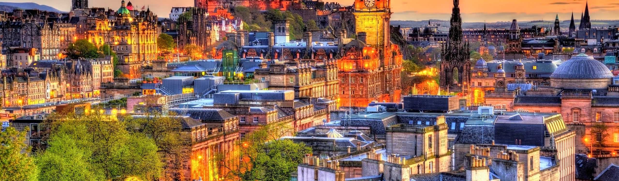 Panoramic sunset view over the historic Edinburgh skyline showing Castle Rock and old town monuments under a golden sky